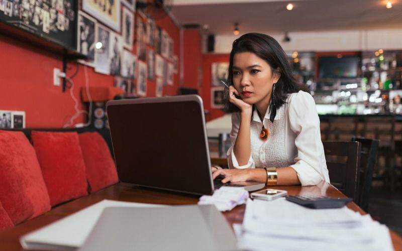 woman using laptop computer, stacks of papers on table
